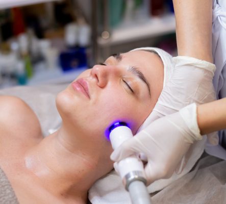 A young beautiful girl lies on the beautician's table and receives procedures with a professional apparatus for skin rejuvenation and moisturizing