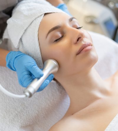 Young woman lying on cosmetologist's table during rejuvenation procedure. Cosmetologist take care about neck and face skin youthfull and wellness. Hardware face cleaning procedure